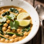 Chickpea spinach curry in white bowl with cilantro and lime