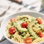 creamy avocado pasta salad in white bowl with basil and tomatoes