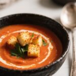 Creamy tomato soup with grilled cheese croutons in a black bowl